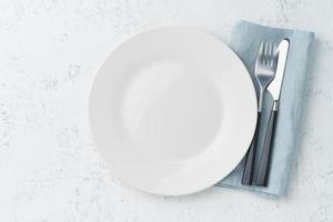 clean empty white plate, fork and knife on white stone table, copy space, mock up, top view. photo