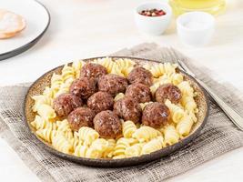Swedish meatballs with fusilli paste on white wooden table, side view