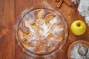 Apple french cake with apples, cinnamon on dark wooden kitchen table, top view