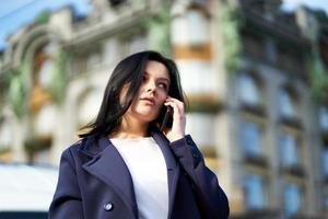 Woman with long hair talking on phone. Autumn or winter, girl in outdoor. Beautiful intelligent brunette in street of Saint-Petersburg in city center, copy space