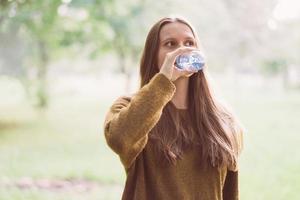 Young beautiful girl drinking water from a plastic bottle on the street in the Park in autumn or winter. A woman with beautiful long thick dark hair quenches her thirst for water on a walk photo