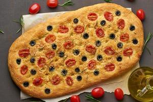 Focaccia with tomatoes, olives and rosemary, side view. Traditional Italian flat bread photo