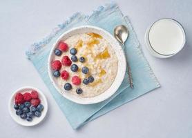 Oatmeal with berries, chia, maple syrup and glass of milk on blue light background