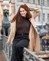 Beautiful serious stylish fashionable smart girl standing on bridge and smiling, St. Petersburg city. Charming thoughtful woman with long dark hair, top shoot.