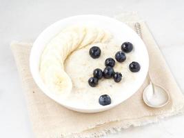 Large bowl of tasty and healthy oatmeal with fruits and berry for Breakfast, morning meal. Side view, white marble table photo