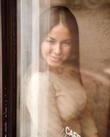 una hermosa chica se sienta en el café y mira por la ventana con cuidado. reflejo de la ciudad en la ventana. mujer morena sonriente con el pelo largo, vertical foto