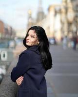 Portrait f beautiful intelligent brunette who walks down street of Saint-Petersburg in city center. Charming thoughtful woman with long dark hair wanders alone, immersed in thoughts photo