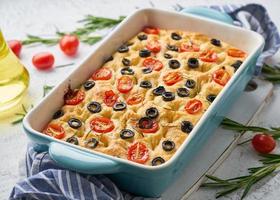 Focaccia with tomatoes, olives and rosemary in blue casserole. Traditional Italian flat bread photo
