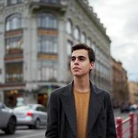 Handsome stylish fashionable man, brunette in elegant gray coat, stands on street in historical center of St. Petersburg. Young man with dark hair, thick eyebrows. photo