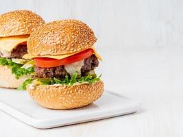 Two hamburgers on white board on white background, hot homemade unhealthy fat food, copy space photo