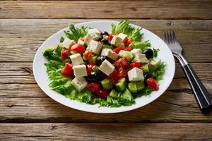 Greek salad on white plate on old rustic wooden table, side view photo