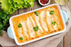 Cannelloni with filling of ground beef, tomatoes, baked with bechamel tomato sauce, top view, old dark wooden background photo