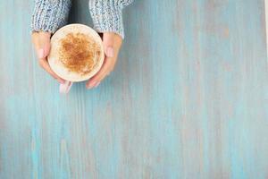 hands holding cup of hot chocolate, blue wooden table, blue cozy sweater, beautiful pink manicure, home style, winter morning, close up, top view, copy space photo