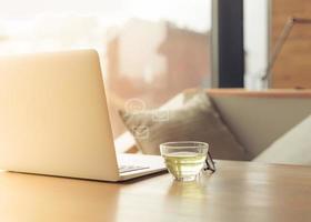 Freelance Desk with open laptop, cup of green tea and glasses on table. Cafe or coworking space. Concept of digital nomads, home office, blogging photo