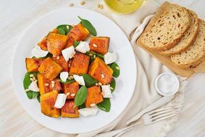 Salad with roasted pumpkin, feta cheese, spinach, nuts with honey and seasonings, top view photo