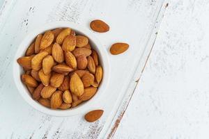 Top view almonds nuts in white bowl on a white wooden cutting board. Wooden background,