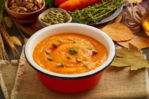 Pumpkin cream soup with seeds and walnuts, side view with autumn leaves for the atmosphere photo