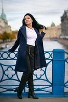 Charming thoughtful fashionably dressed woman with long dark hair travels through Europe, standing in city center of St. Petersburg. A beautiful girl wanders alone through autumn streets