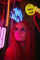 Girl in neon lights, beautiful woman in sunglasses, with pink hair, with dreadlocks pigtails photo