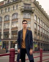 apuesto hombre de moda con estilo, morena con elegante abrigo gris, se encuentra en la calle en el centro histórico de st. petersburgo joven de cabello oscuro, cejas pobladas.