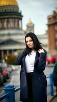 Charming thoughtful fashionably dressed woman with long dark hair travels through Europe, standing in city center of St. Petersburg, thoughtful woman with long dark hair wanders alone photo