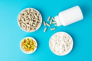 Blue background of large group of assorted capsules, pills and tablets in bottle and bowl photo