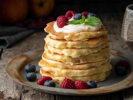 Pancake with vanilla cream, blueberries and raspberries. Side view, macro, close-up. Dark moody old rustic wooden background.