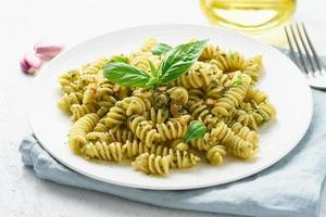 fusili pasta with basil pesto and herbs, italian cuisine, gray stone background, closeup