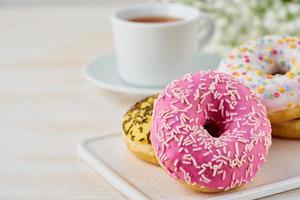 Doughnuts and tea. Bright, colorful junk food. Light beige wooden background. Side view, close up. photo