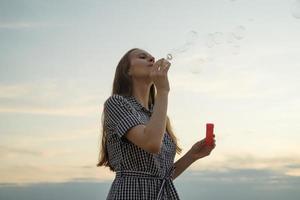 Teenager blowing soup bubbles, concept of fun and joy, sky and clouds on background photo