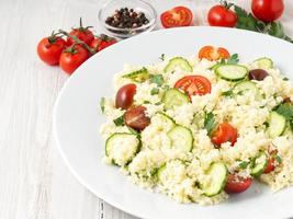 fresh diet vegetable salad with couscous, tomatoes, cucumbers, parsley, white wooden table, side view
