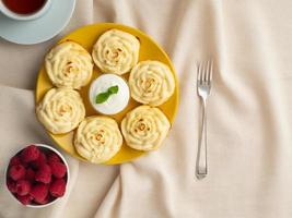 Diet cheese pancakes, rose shape, on yellow plate with tea, raspberry on textile linen napkin photo