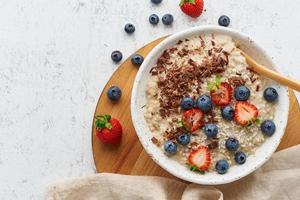 Oatmeal porridge rustic with berries and chocolate, dash diet, on white wooden background top view photo