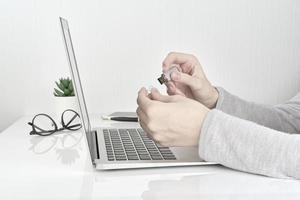 persona abriendo flash usb junto a la computadora portátil, concepto de trabajo de oficina en el fondo de la pared blanca foto