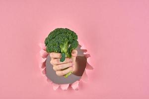 The idea of making decision for healthy lifestyle, broccoli as a sign of wellness on pink background with a ripped hole, closeup photo