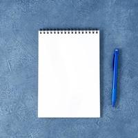 The open notepad with clean white page on aged dark blue stone table, top view