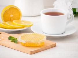 White Cup with tea, lemon slices and honey in honeycomb on white wooden table, side view photo