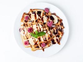 Belgian curd waffles with raspberries, banana, chocolate syrup. Breakfast with tea on white background, top view, macro photo