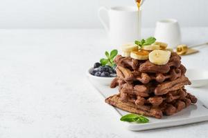 Chocolate banana waffles on white table, copy space, side view. Sweet brunch photo