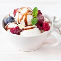 Balls of vanilla ice cream in mug with raspberry and blueberries, chocolate photo