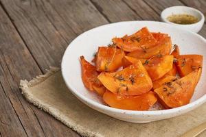 calabaza asada, piezas en plato con miel y condimentos, antigua mesa rústica de madera oscura foto