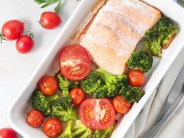 Fish salmon baked in oven with vegetables, broccoli. Healthy diet food, white marble backdrop, top view, close-up photo