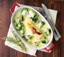 Chicken fillet baked with broccoli in bechamel sauce on dark wooden table. Healthy food photo