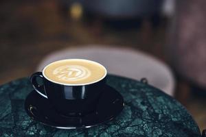 una taza de capuchino con espuma sobre una mesa de mármol cerca de la ventana en un pequeño y acogedor café. bebida con leche vegetal, avena, coco foto