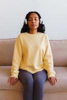 African-American female sitting on couch and listening to music in headphones. Breathing therapy