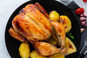 pollo entero a la parrilla en plato negro sobre mesa blanca, carne al horno con patatas. vista superior, primer plano