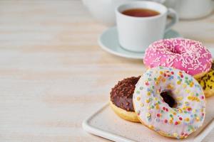 Doughnuts and tea. Bright, colorful junk food. Light beige wooden background. Side view, close up. photo