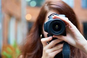 Beautiful stylish fashionable girl holds a camera in her hands and takes pictures. Woman photographer with long dark hair photo