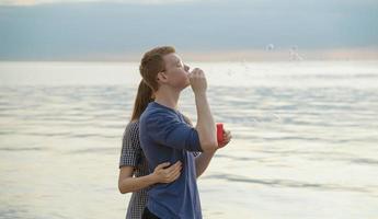 pareja adolescente soplando burbujas de sopa en la playa, el océano y el cielo en el fondo