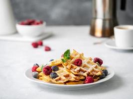 Belgian waffles with raspberries, blueberries, curd and coffee, side view. Healthy homemade breakfast, light concrete background